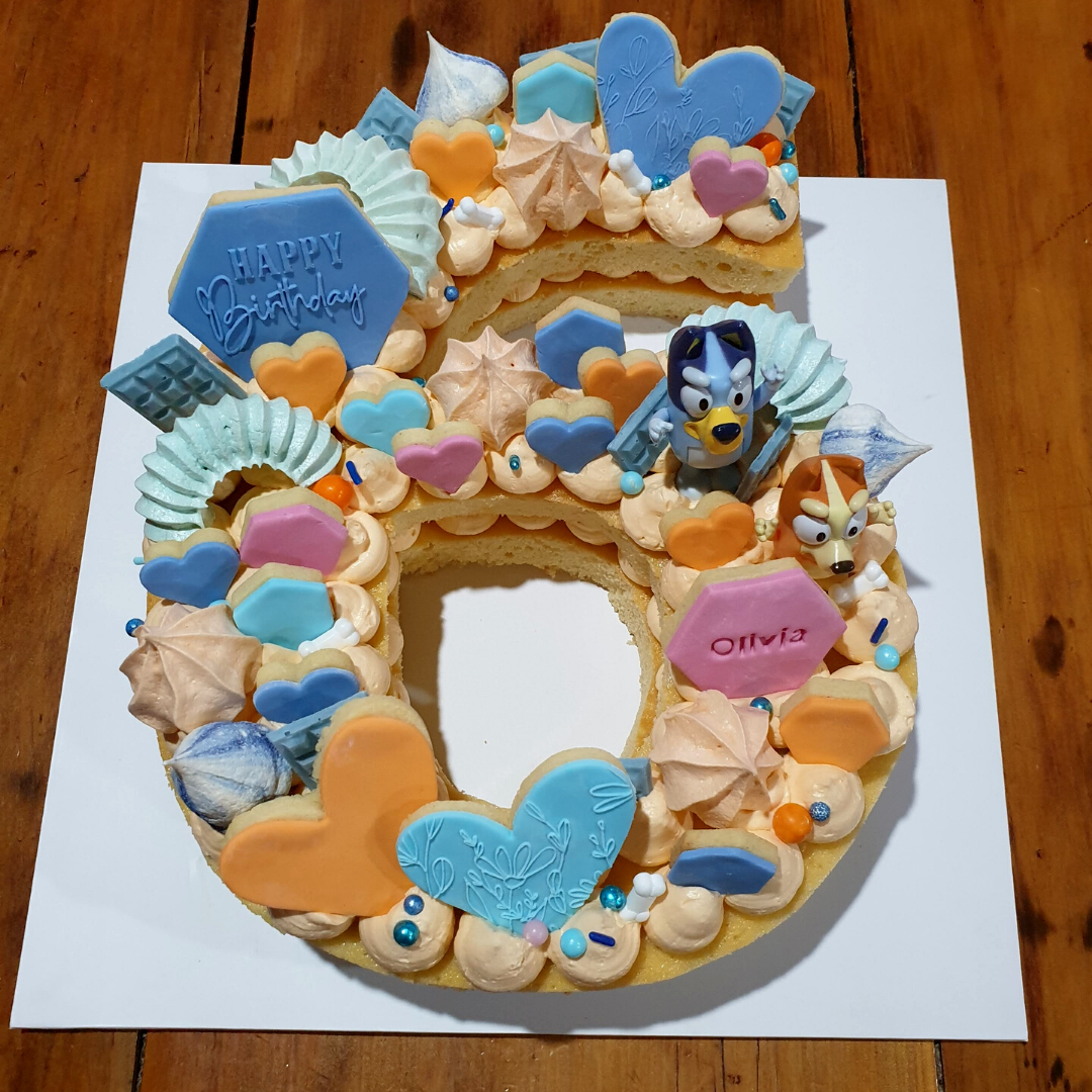 A Bluey themed child&#39;s birthday cake.  The number 6 was cut out of the cake with the DoughCuts reusable number 6 baking template.